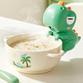 Soplador de sopa con forma de dinosaurio verde enfriando un bol de papilla